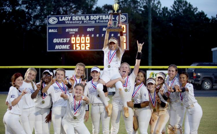 The Lady Devils hold the region championship trophy in front of the scoreboard after defeating Commerce 8-0 at Wesley King Field Oct. 5. (Photo by Wells) 